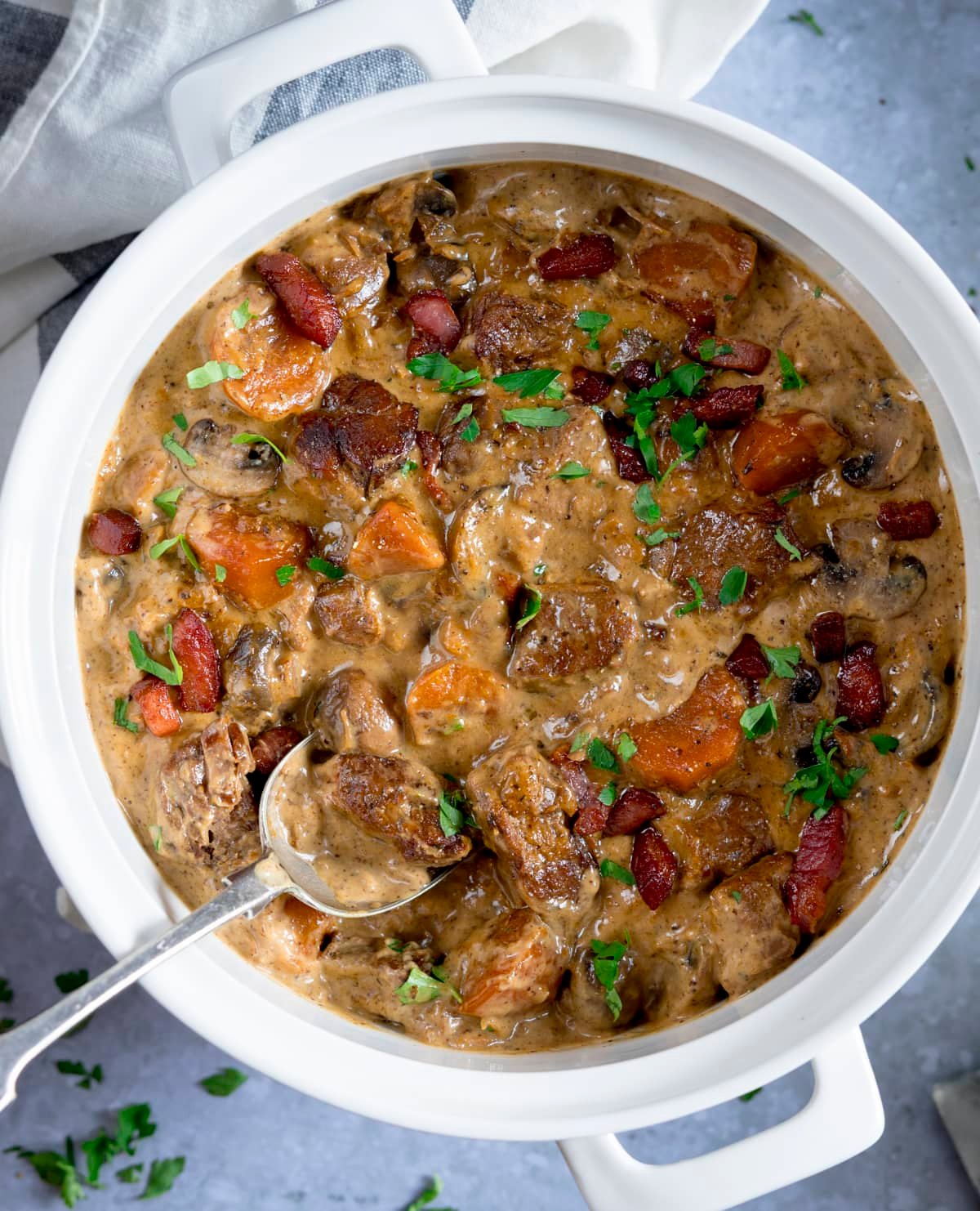 Overhead image of creamy slow-cooked pork casserole in a white casserole dish on a light blue background.