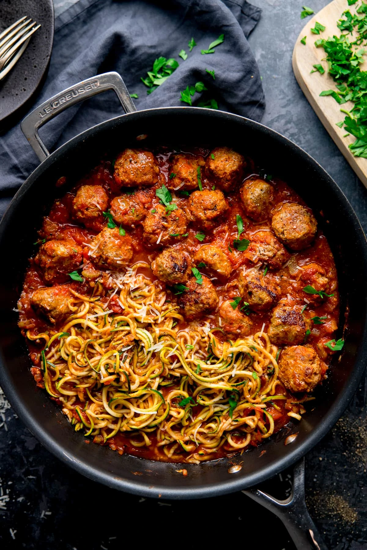 Turkey meatballs and courgetti in a pan topped with parsley, on a dark background.