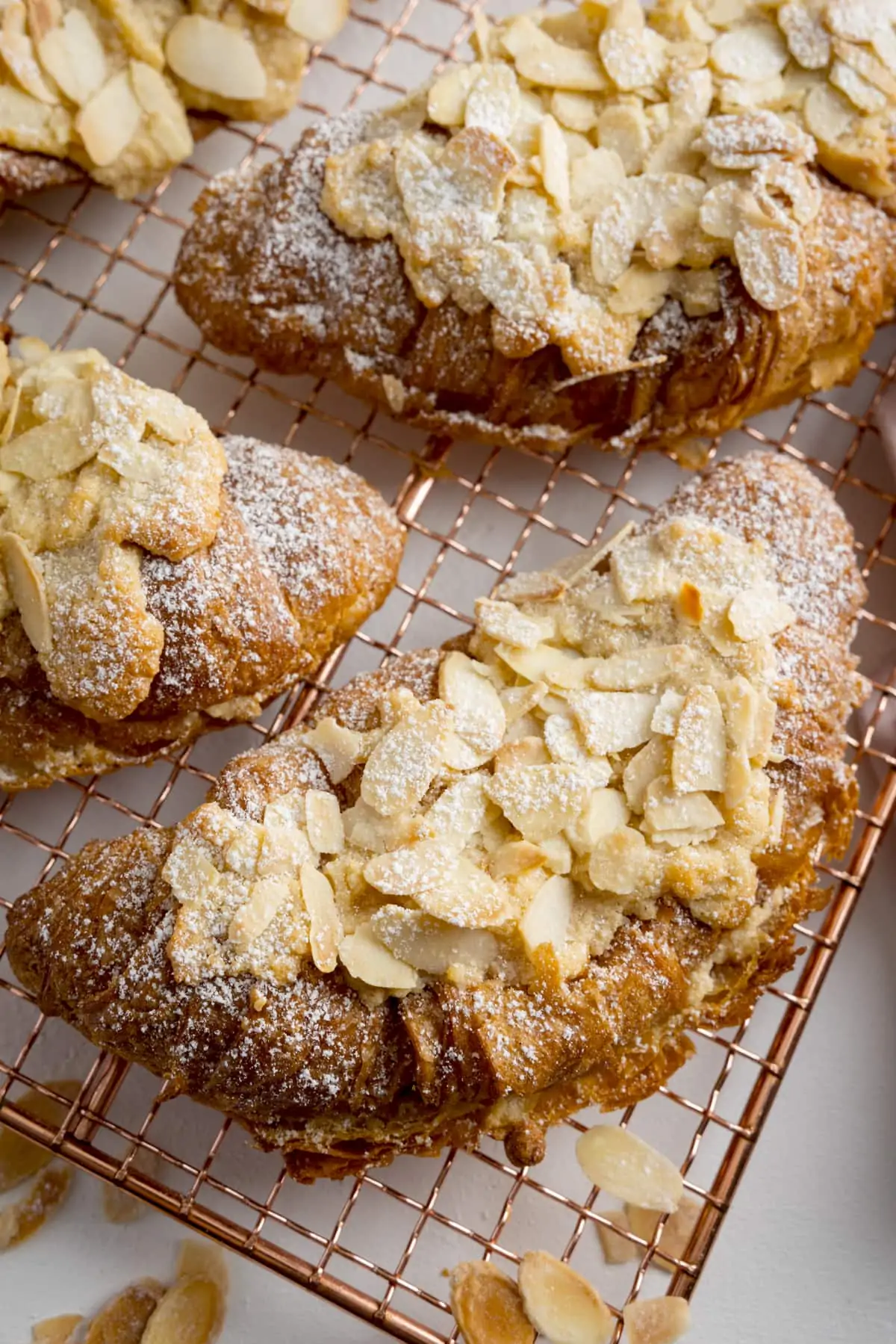 Almond croissants on a gold wire cooling rack, on a white background.