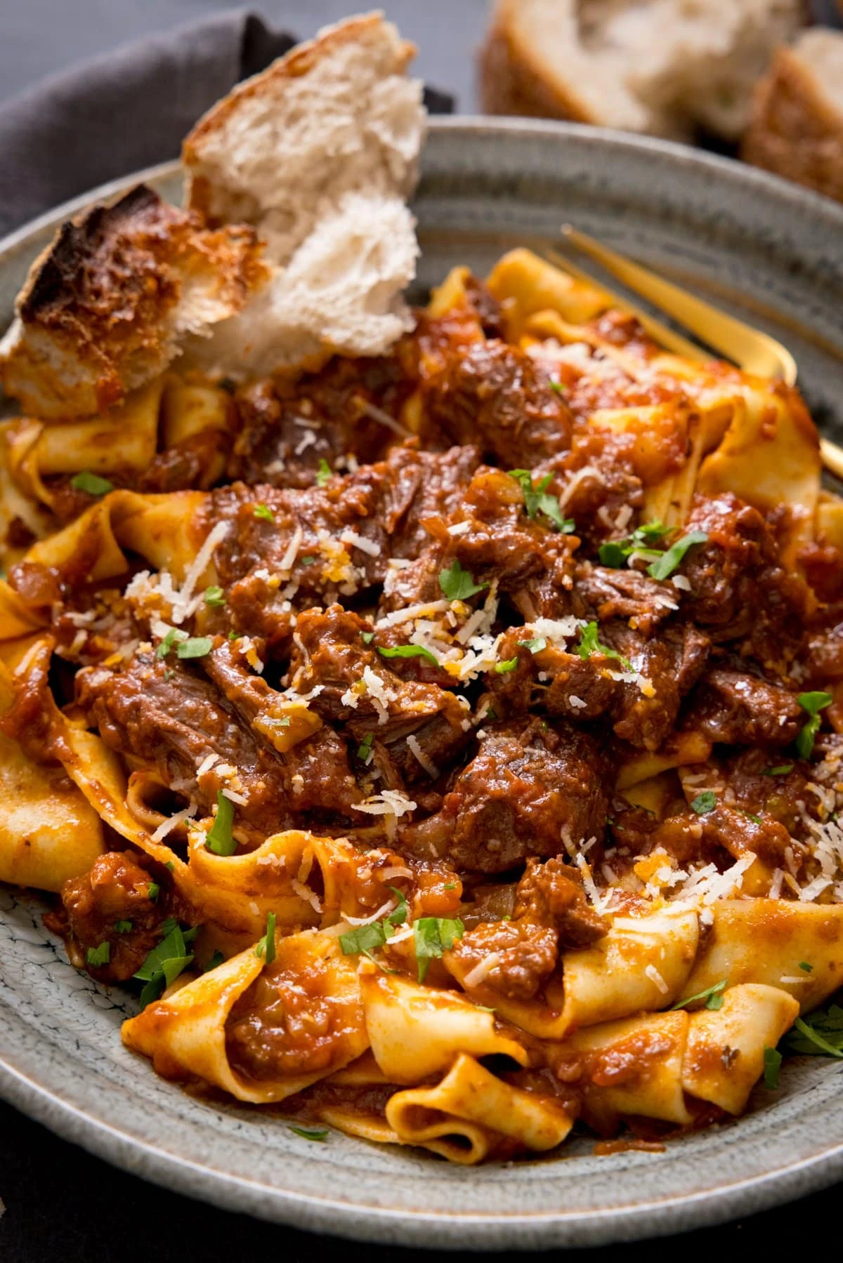 Beef ragu with pappardelle in a bowl with a chunk of bread.