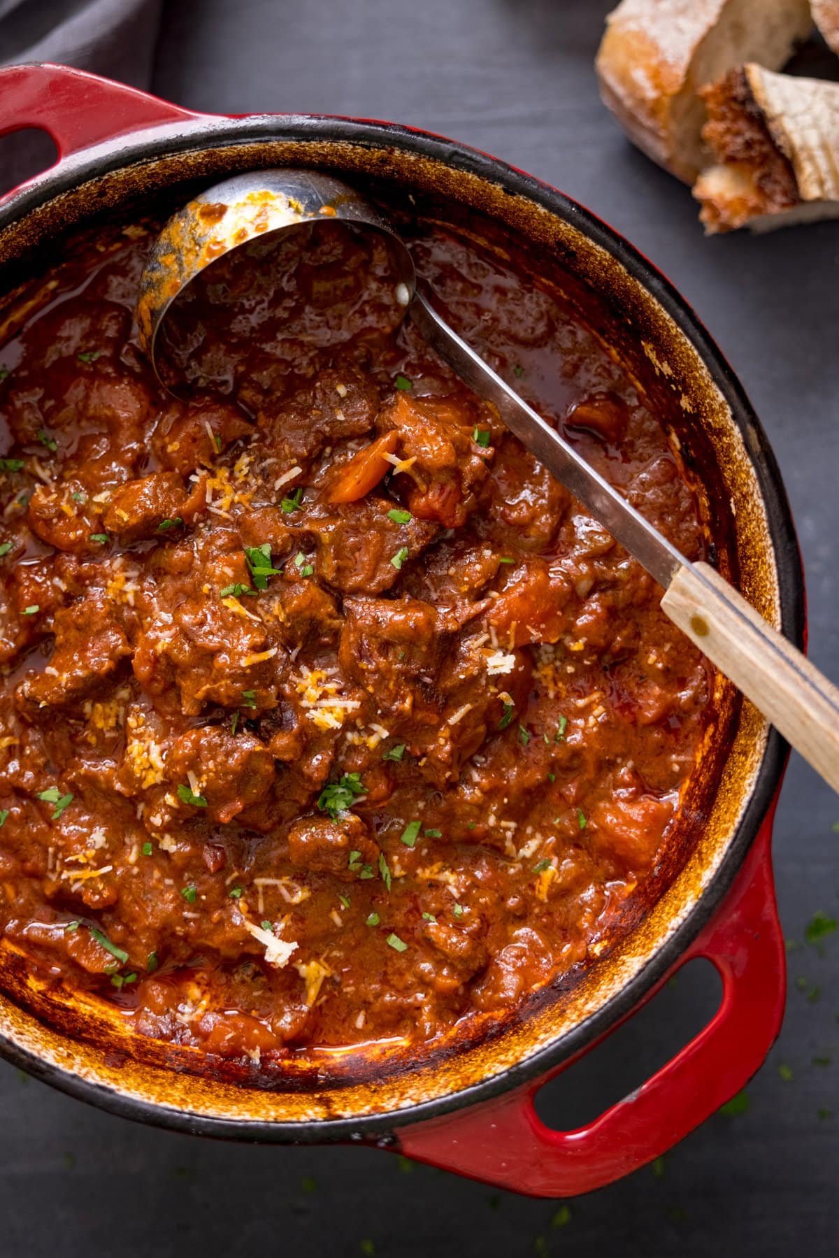 Overhead image of beef ragu in a red cast iron pan. There is a ladle in the pan.