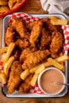 A tray of Crispy Chicken Goujons with Garlic Chilli Dip and crinkle-cut chips on red checkered paper, served with a pot of dipping sauce.