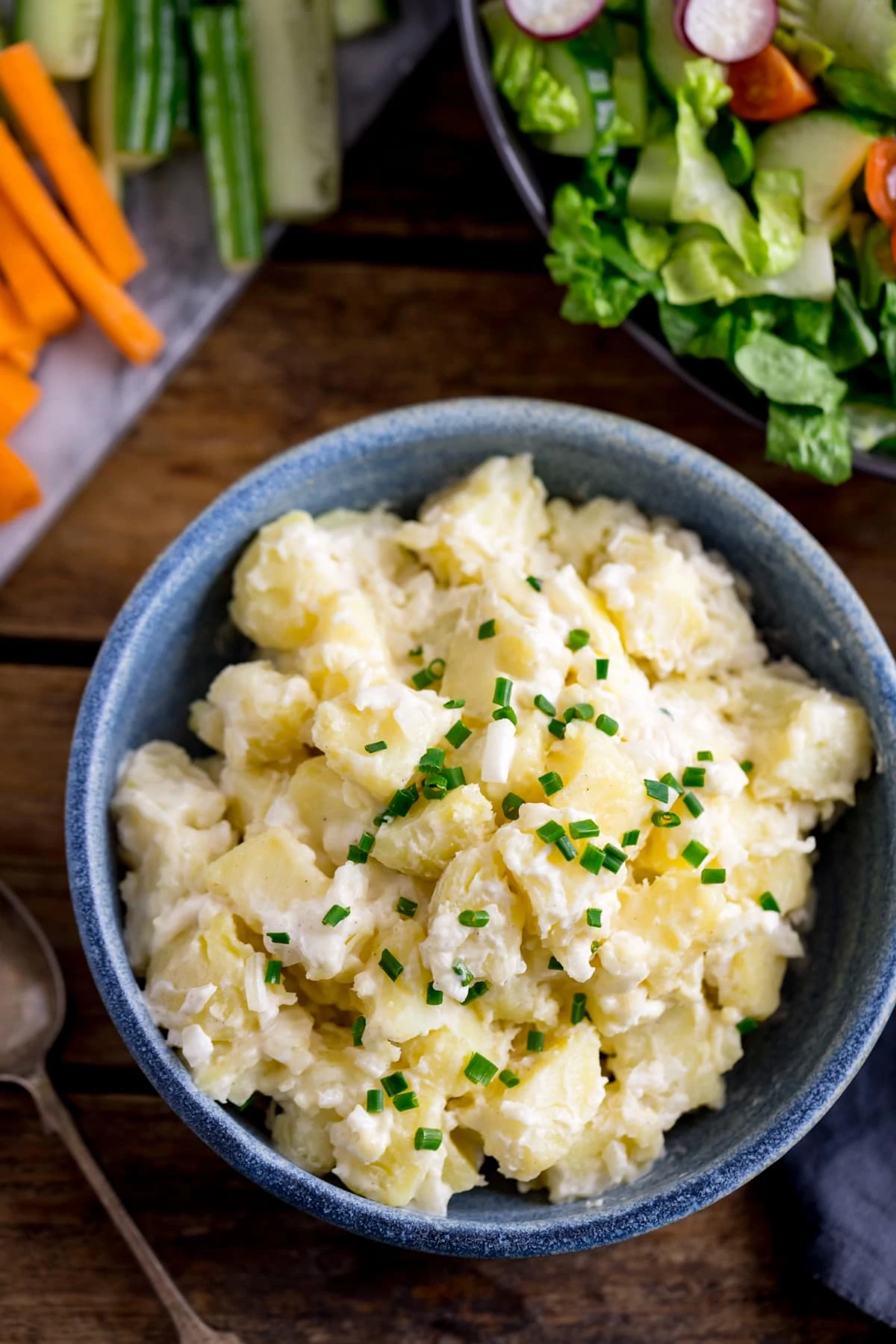 Overhead image of potato salad in a blue bowl with vegetables in the background