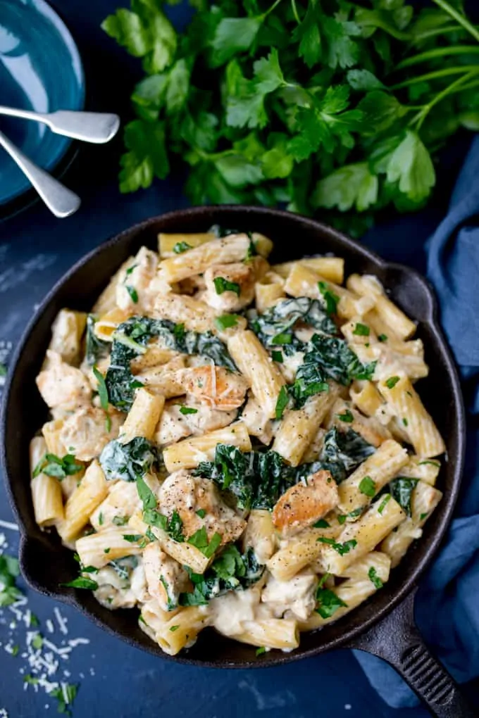 One Pot Rigatoni Alfredo with Chicken and Kale in a creamy, rich, garlic and parmesan sauce on a blue background with parsley in the background
