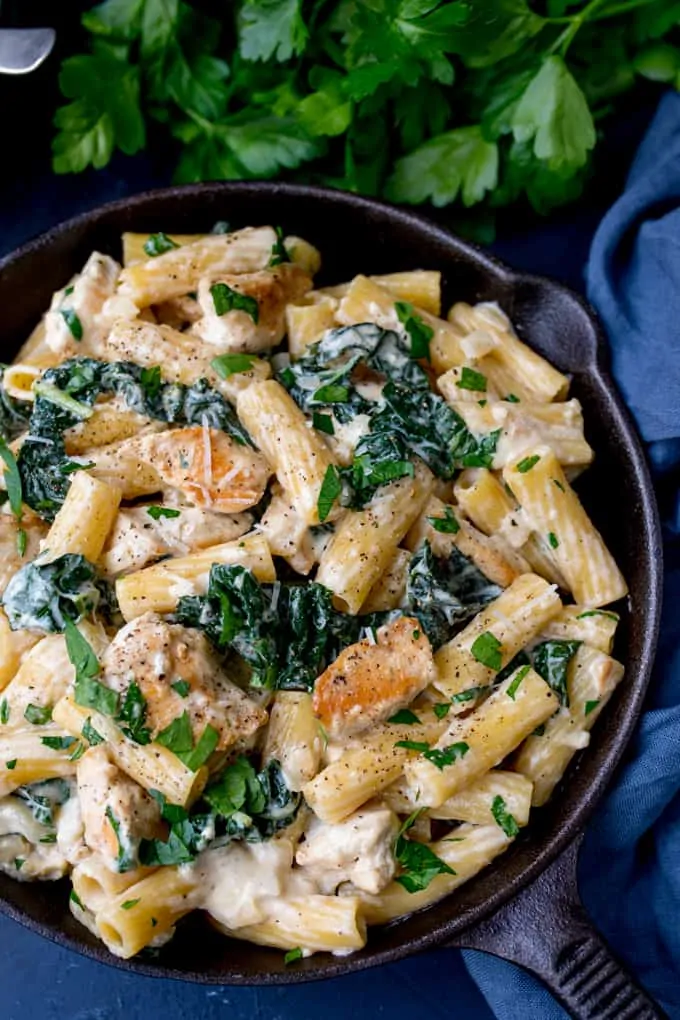 Rigatoni Alfredo with Chicken and Kale in a cast iron pan on a blue background