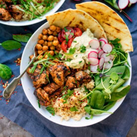 spicy chicken, chickpeas, couscous, leaves, radish, hummus and flatbreads in a bowl