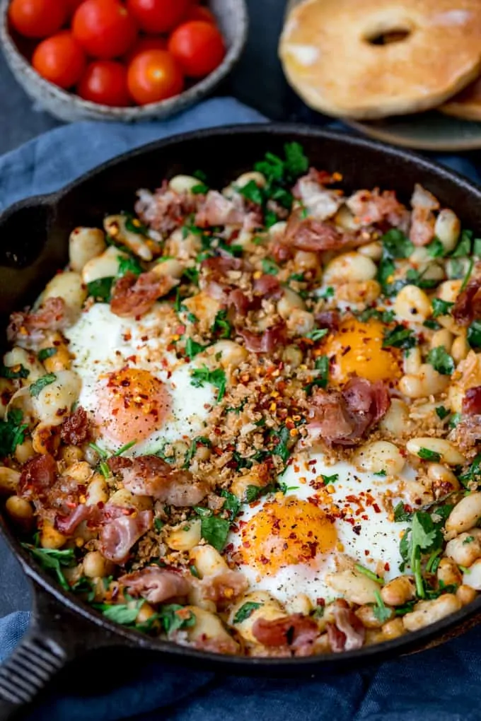 Spicy Egg Breakfast with Smashed Beans and Pancetta with tomato's and a bagel in the background