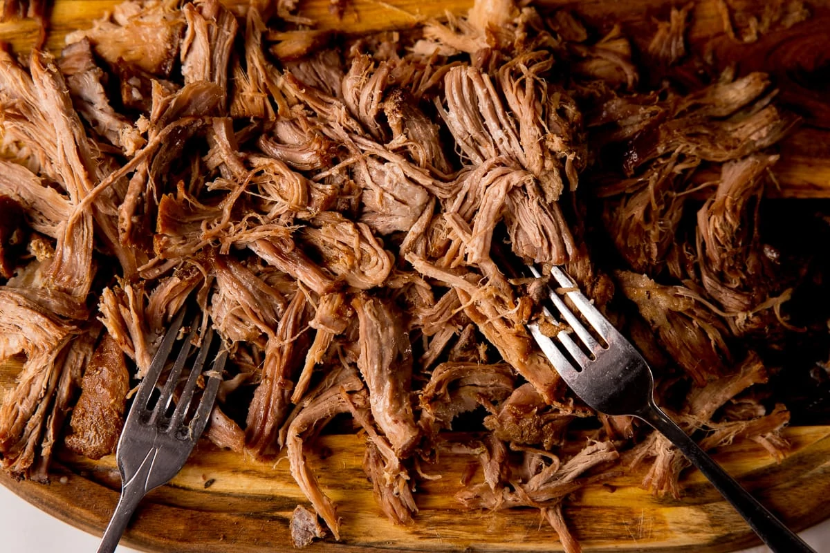 Shredded pork on a board with two forks
