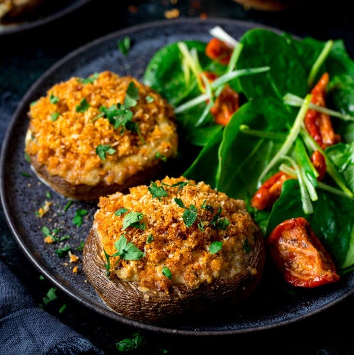 Square image of Stuffed mushrooms on a black plate with salad