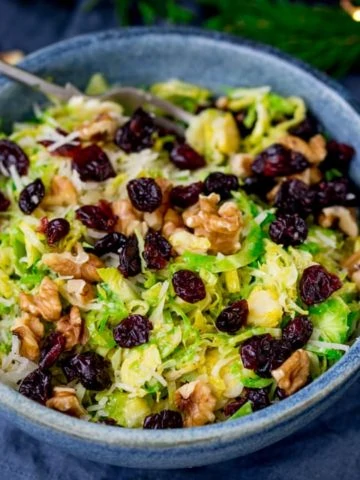 Square image of a bowl with shaved sprouts topped with cranberries, walnuts and parmesan in a honey mustard dressing