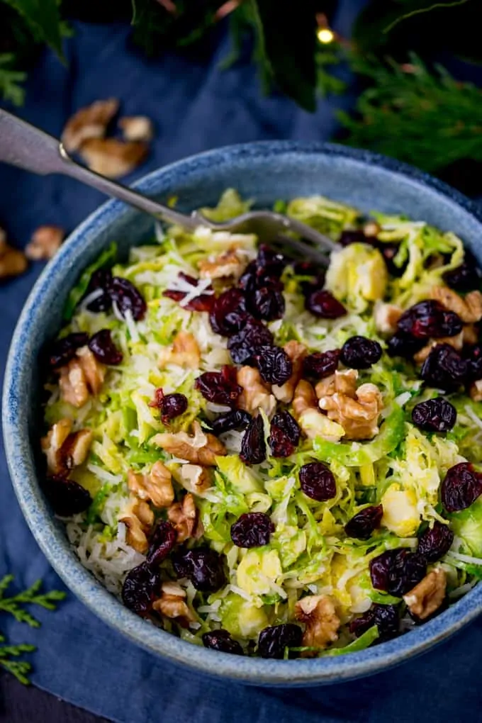 Blue bowl with shaved sprouts topped with cranberries, walnuts and parmesan