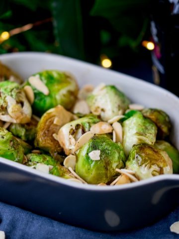 Close up image of roasted sprouts with honey, balsamic and almonds in a grey and white dish.