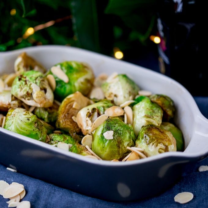 Close up image of roasted sprouts with honey, balsamic and almonds in a grey and white dish.