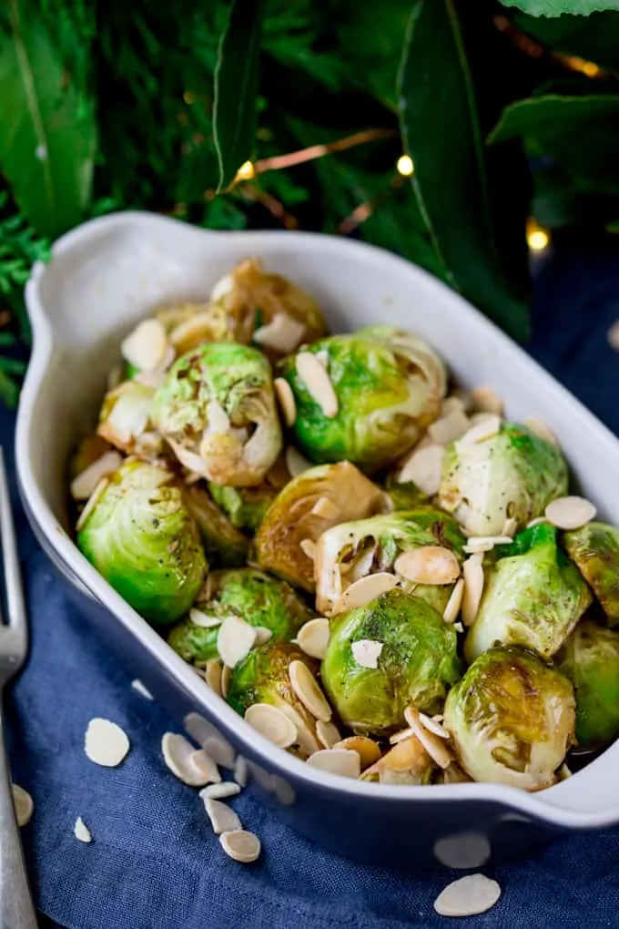 Roasted sprouts with honey, balsamic and almonds in a grey and white dish.