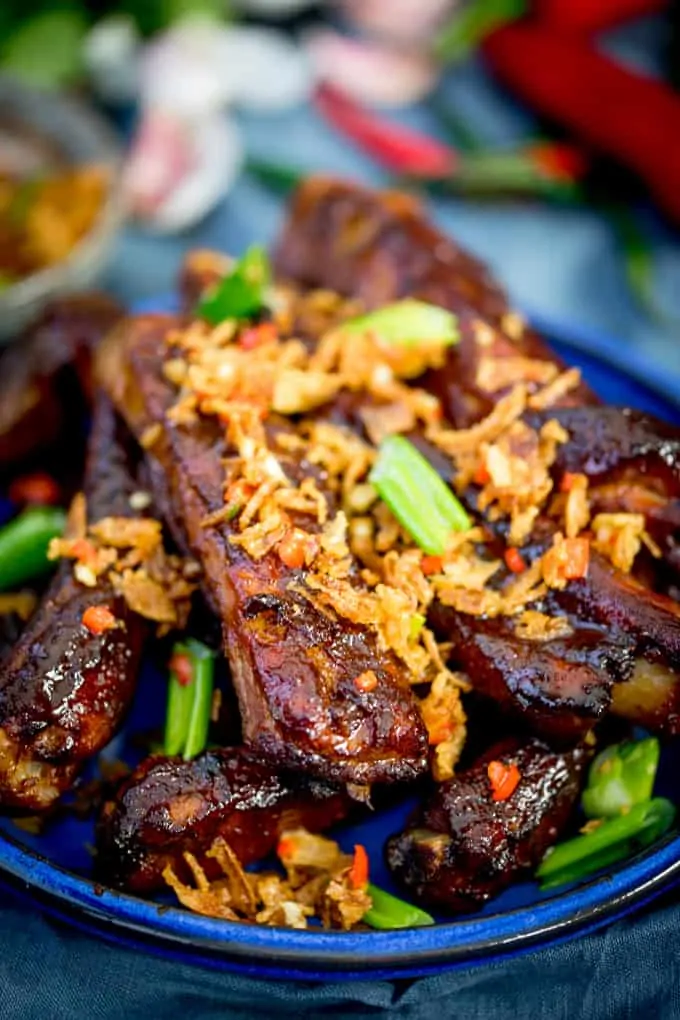Close up of Oven Baked Asian Ribs with Crispy Onions on a blue plate with spring onions