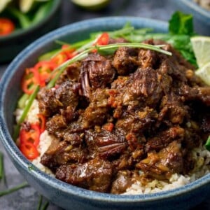 Beef rendang in a blue bowl with rice, chillies and greens