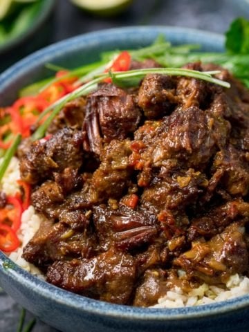 Beef rendang in a blue bowl with rice, chillies and greens