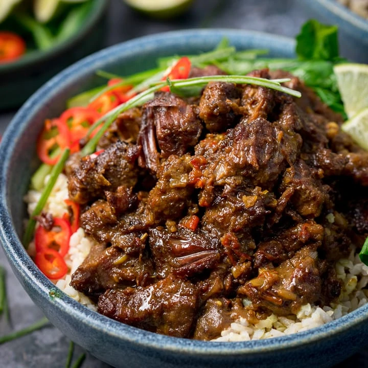 Beef rendang in a blue bowl with rice, chillies and greens
