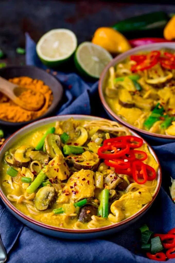 side on photo of 2 bowls of Chicken Noodle Soup with Turmeric on a dark background with spices, chillis and limes in the background 