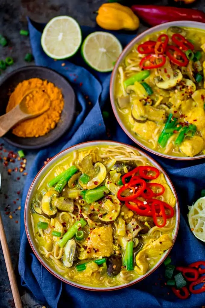 overhead photo of 2 bowls of Chicken Noodle Soup with Turmeric on a dark background with spices and limes in the background 