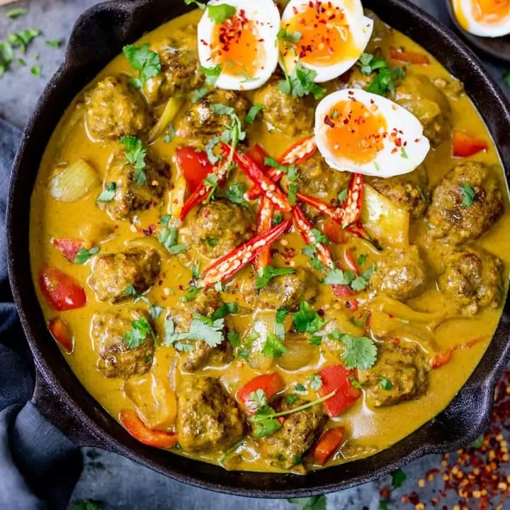 Meatballs with a Chinese Curry Sauce in a cast iron pan with 3 slices of boiled egg in the top right corner.