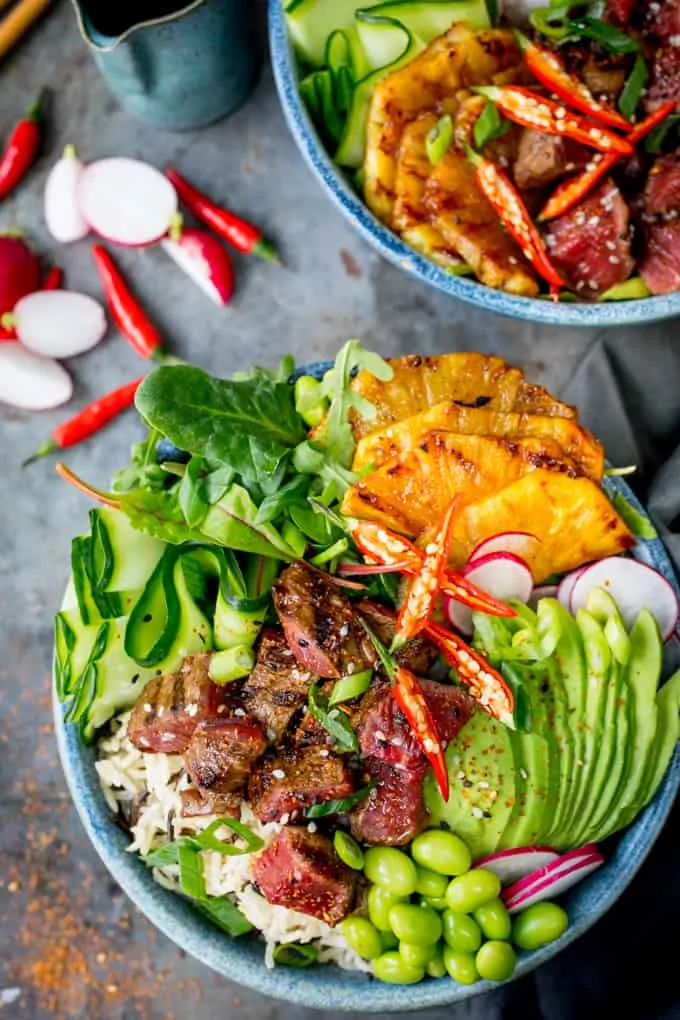 Overhead photo of two steak poke bowls in blue bowls with avocado and chillies.