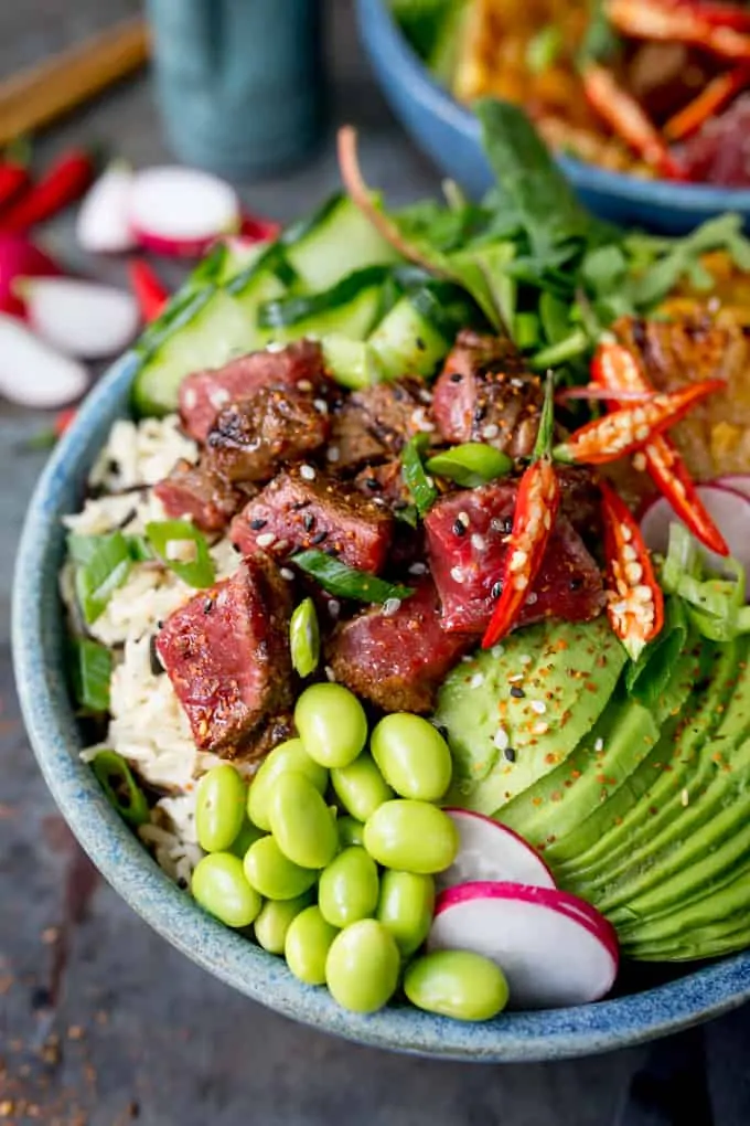 Close up overhead shot of seared steak poke bowl in a blue bowl with avocado and edamame beans