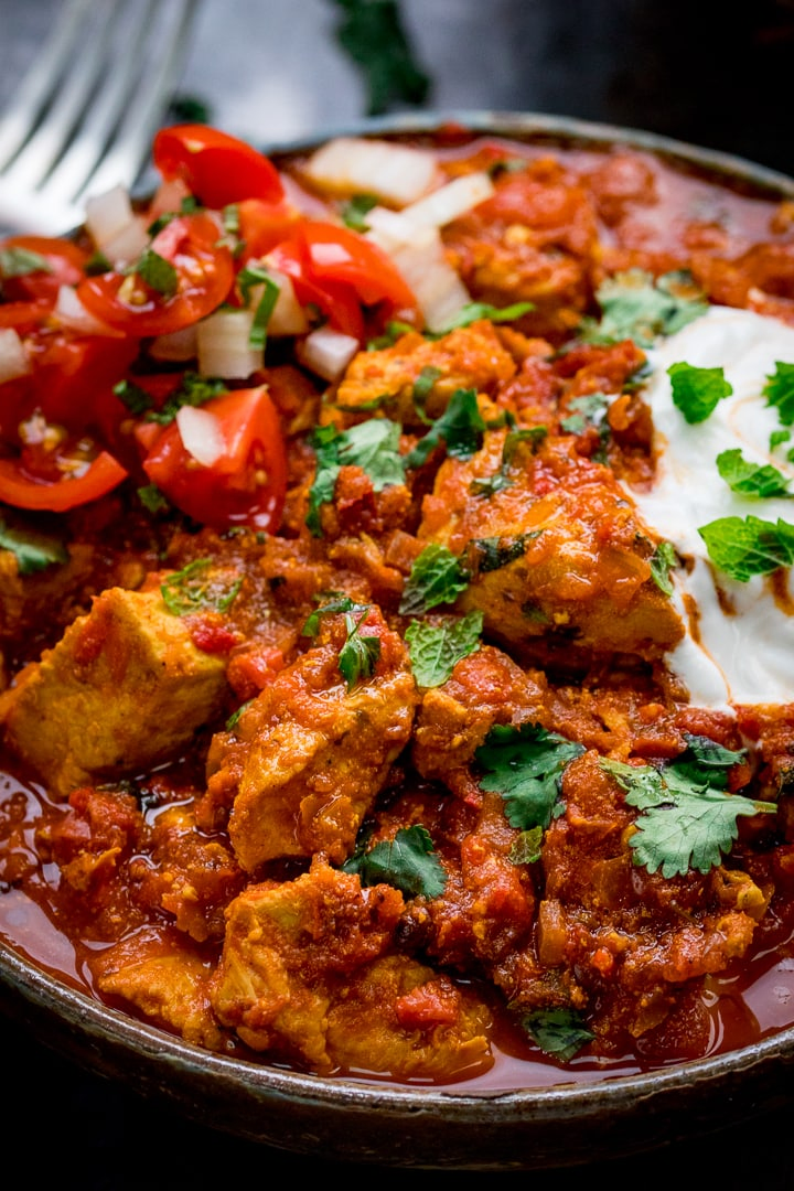 close up image of Spicy Chicken Rogan Josh with yogurt and a bowl of chopped tomatoes and onions