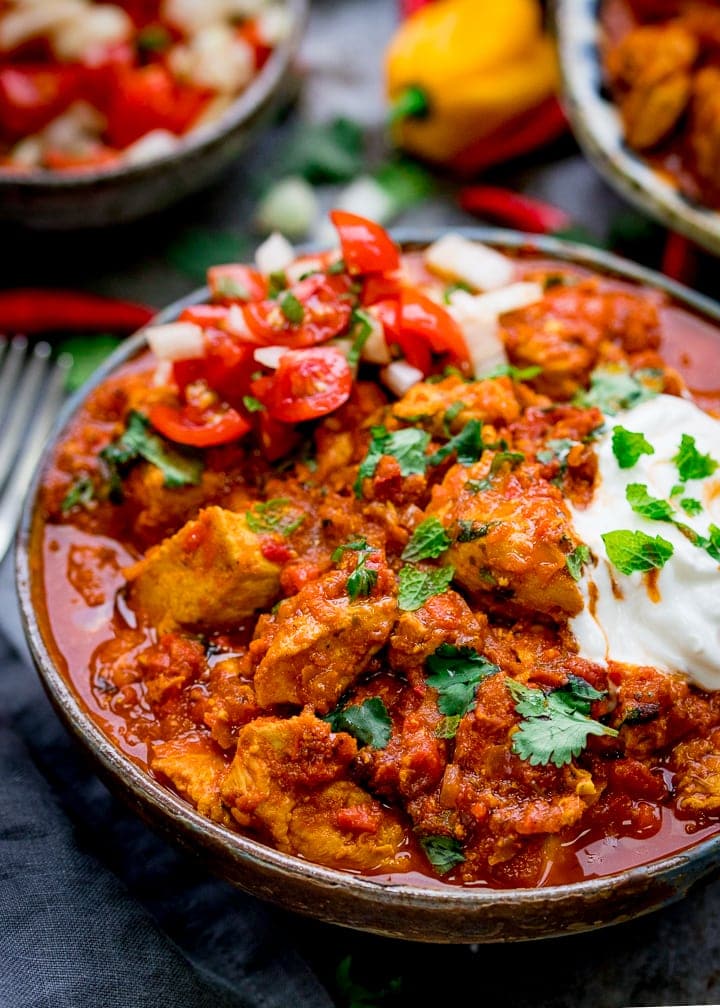 Close up photo of Healthier Slow Cooked Spicy Chicken Rogan Josh in a stone bowl with yogurt and chopped tomatoes and onions as a garnish