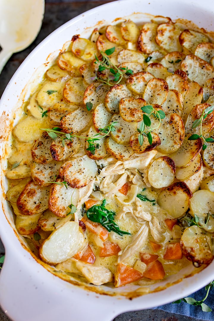 Close up overhead shot of Creamy Chicken and Potato Bake with extra veggies in a grey and white casserole dish with a scoop taken out and the spoon in the background