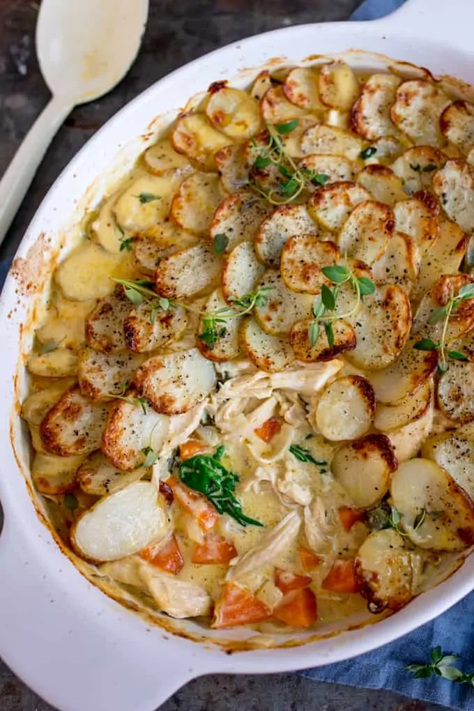 Close up overhead shot of Creamy Chicken and Potato Bake with extra veggies in a grey and white casserole dish with a scoop taken out and the spoon in the background