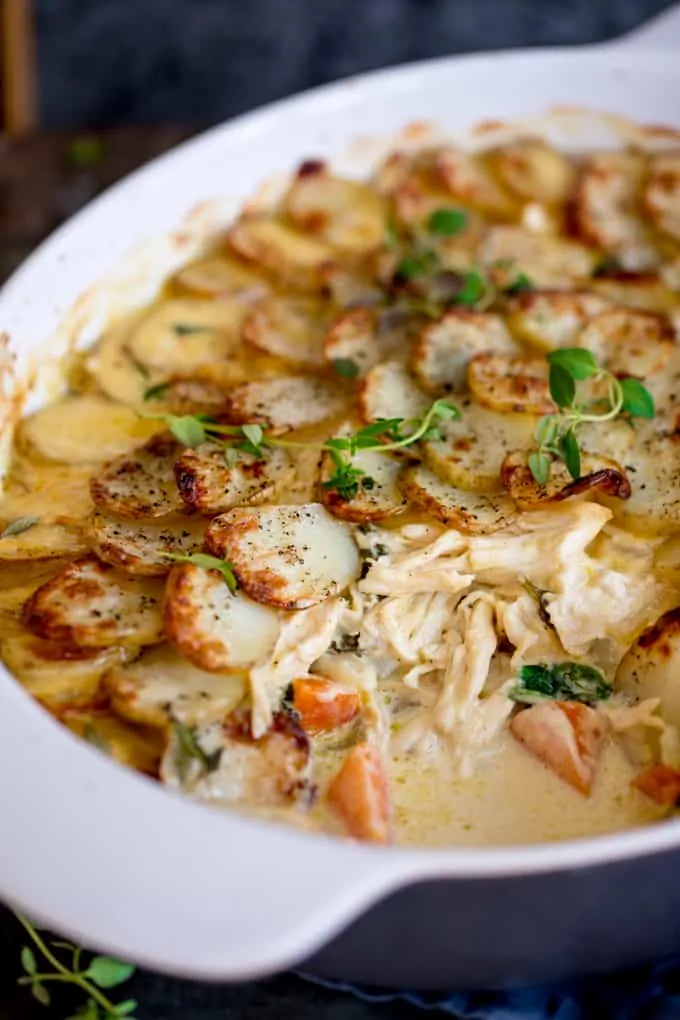 Close up shot of Creamy Chicken and Potato Bake with extra veggies in a grey and white casserole dish with a scoop taken out