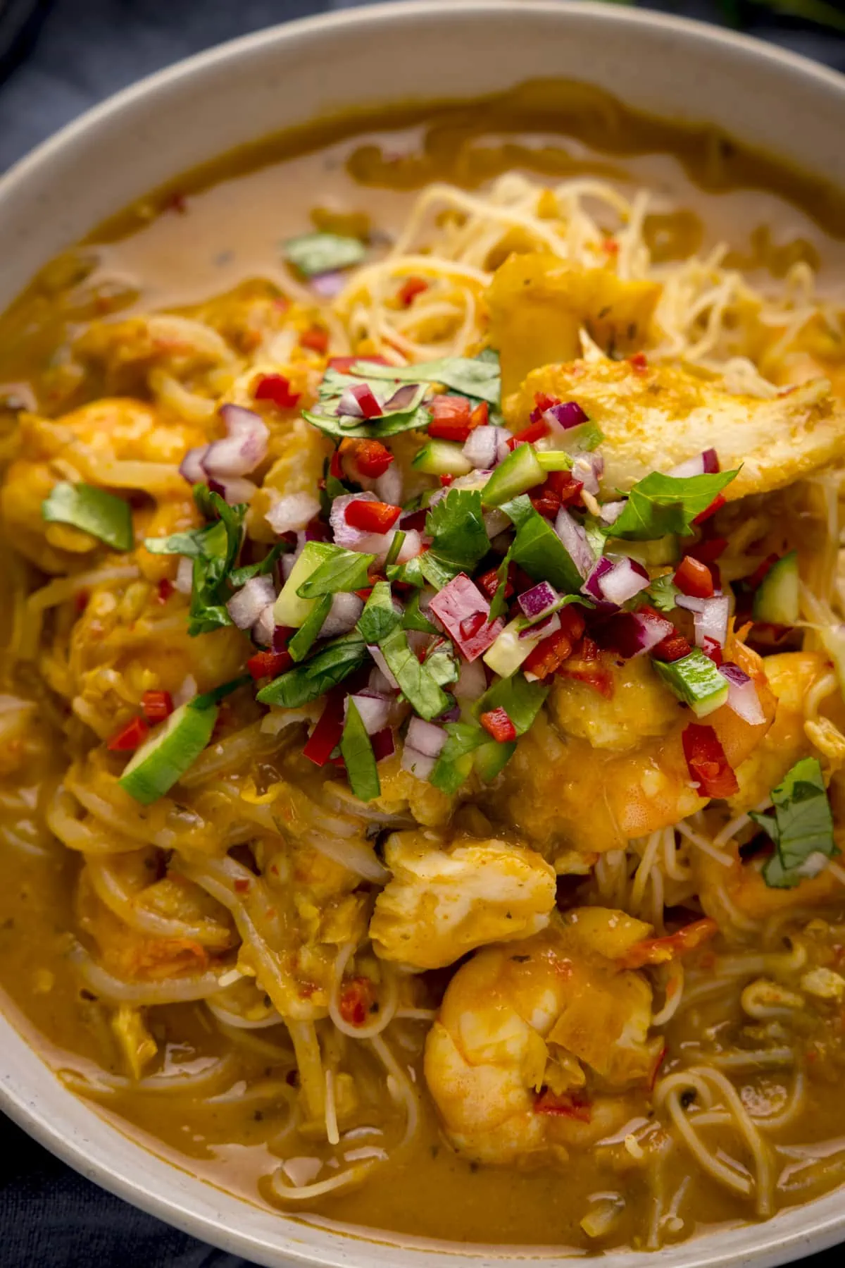 Close up of seafood laksa in a white bowl topped with a chilli-coriander and red onion garnish.