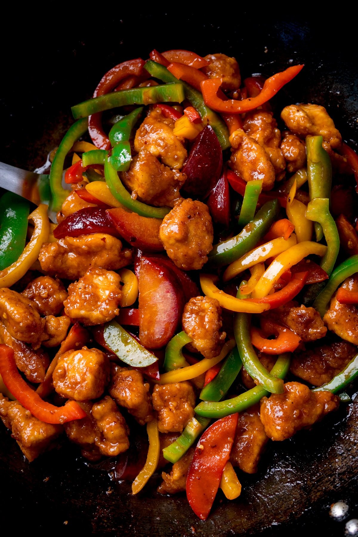 Close up overhead image of Chinese plum chicken stir fry with sliced peppers in a wok.
