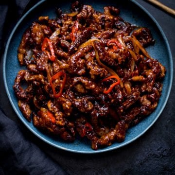 Square image of crispy chilli beef in a blue bowl