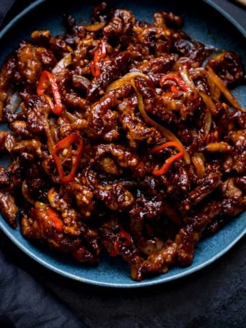 Square image of crispy chilli beef in a blue bowl