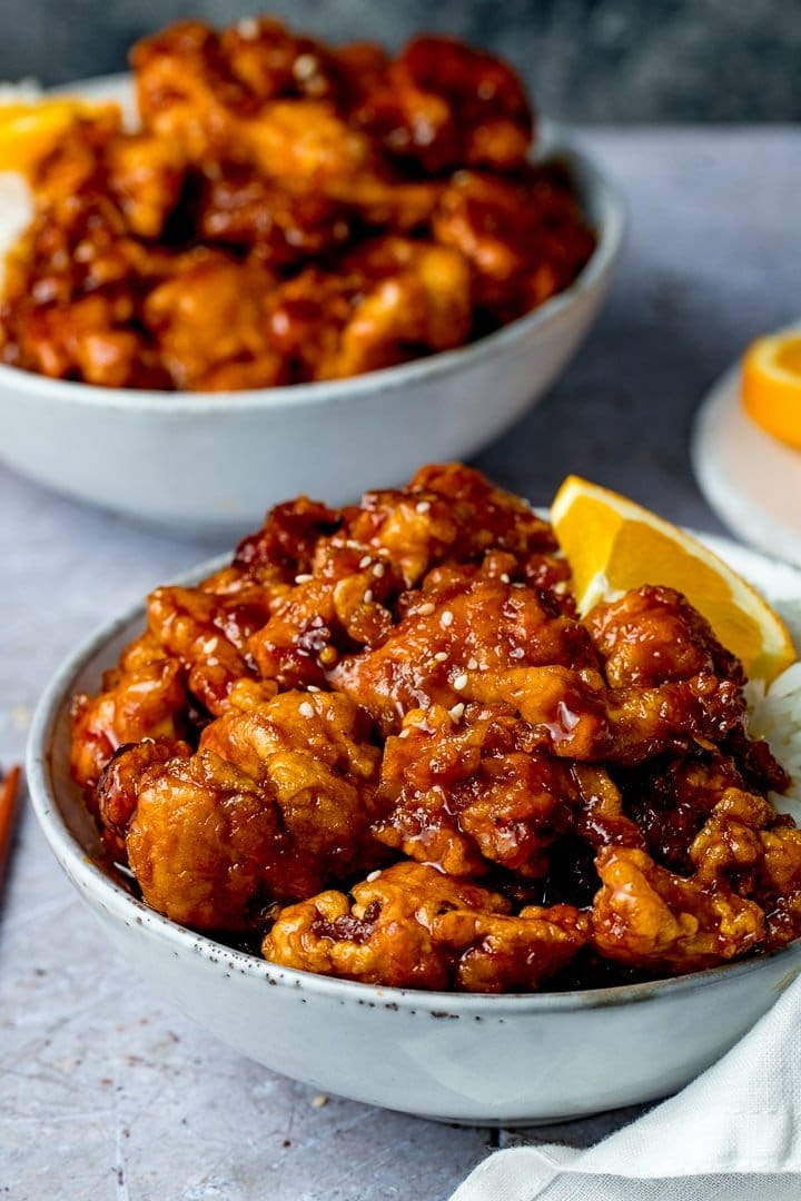 Close up image of crispy orange chicken in a grey bowl. Further bowl in the background.