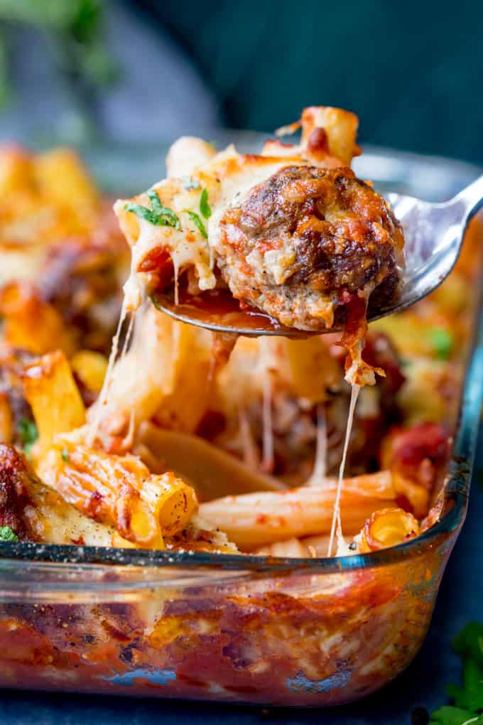 A spoonful of meatball and pasta bake behind lifted from the dish. Cheese is stretching.
