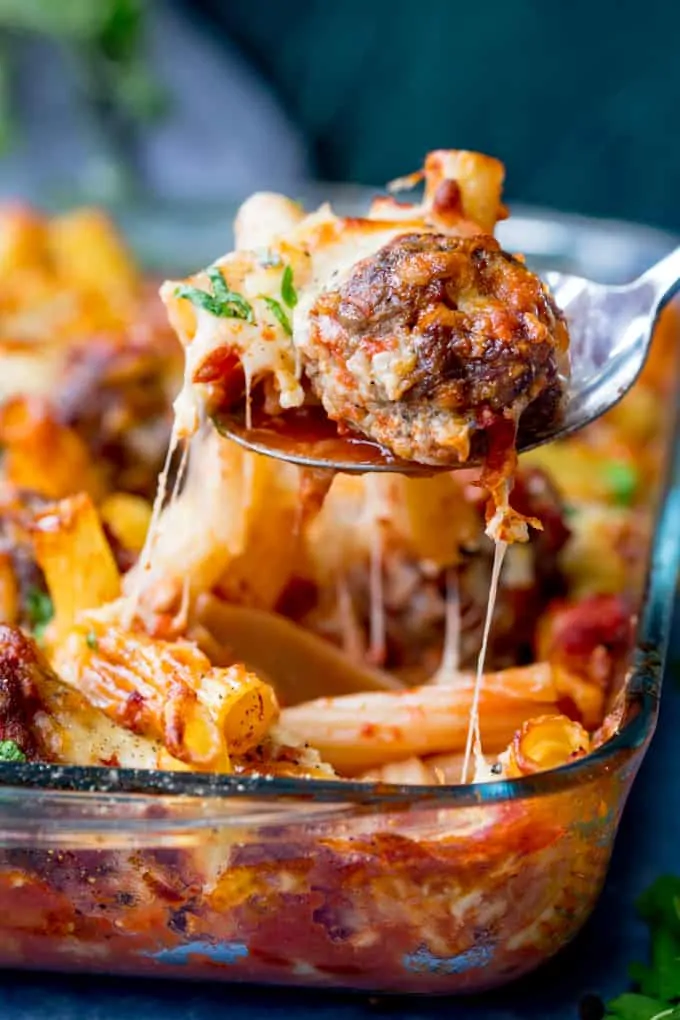 A spoonful of meatball and pasta bake behind lifted from the dish. Cheese is stretching.