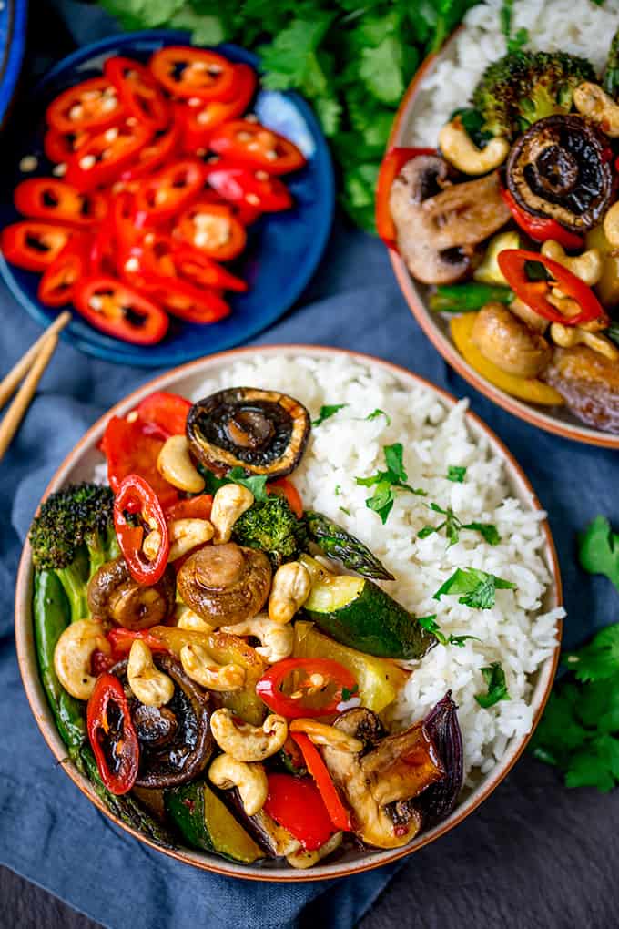 Overhead shot of a bowl of vegetables in asian-style sauce with rice, cashew nuts and sliced chillies.