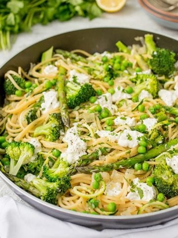 Pan of spaghetti with spring vegetables and goats cheese and lemon slices