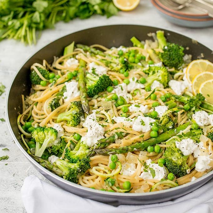 Pan of spaghetti with spring vegetables and goats cheese and lemon slices