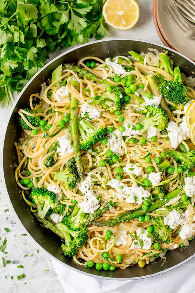 Overhead of pan of spaghetti with spring vegetables and goats cheese