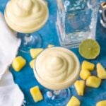 Square overhead image of two glasses of dole whip margarita on blue background.