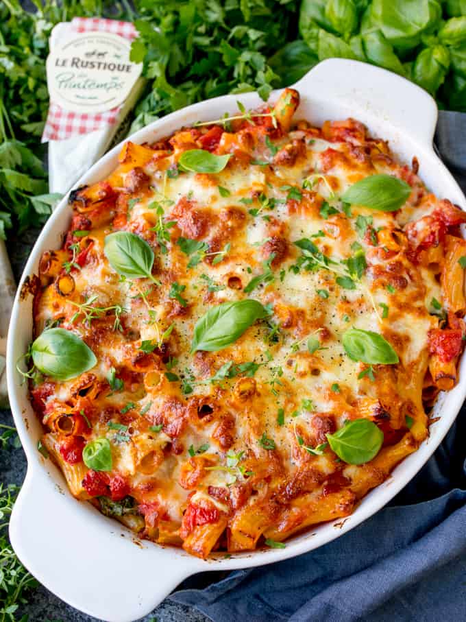 Overhead shot of sausage, chorizo and brie pasta bake with fresh herbs on top. Herbs scattered around the dish. Wedge of Brie in the top of the frame.