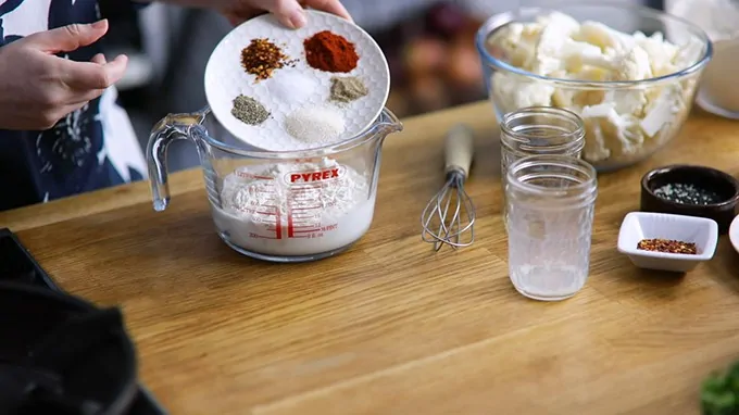 Spices being poured from a plate to a jug to make coating for baked cauliflower wings