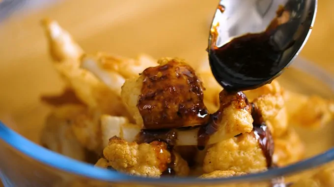 Asian style sauce being poured over baked cauliflower florets