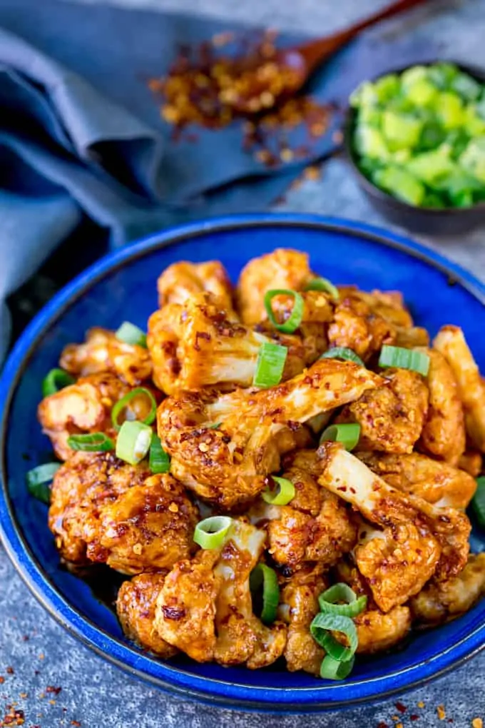 Asian cauliflower wings on a blue plate with spring onions sprinkled on top