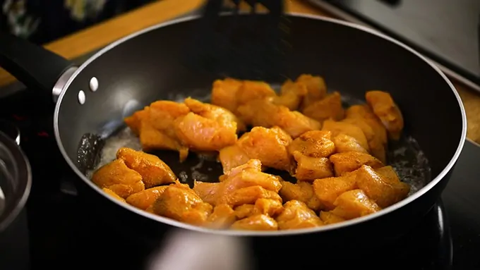 chicken frying in a pan with spices