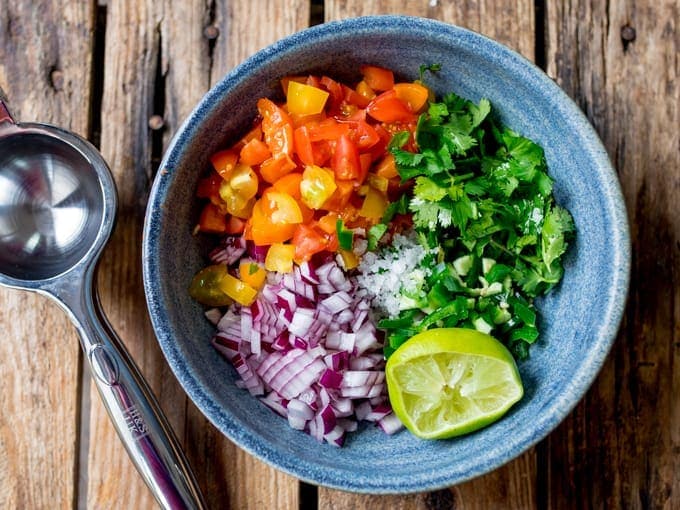 Blue bowl of ingredients on wooden background for pico de gallo. Includes tomatoes, coriander, red onion, jalapeno, lime and salt